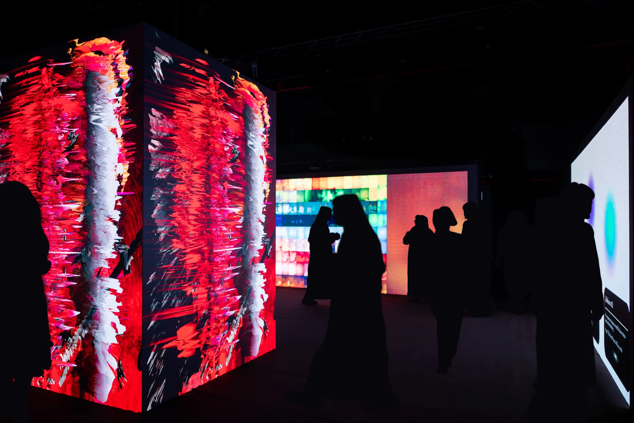 Visitors in silhouette moving between glowing LED installations at Outliers, Abu Dhabi Art