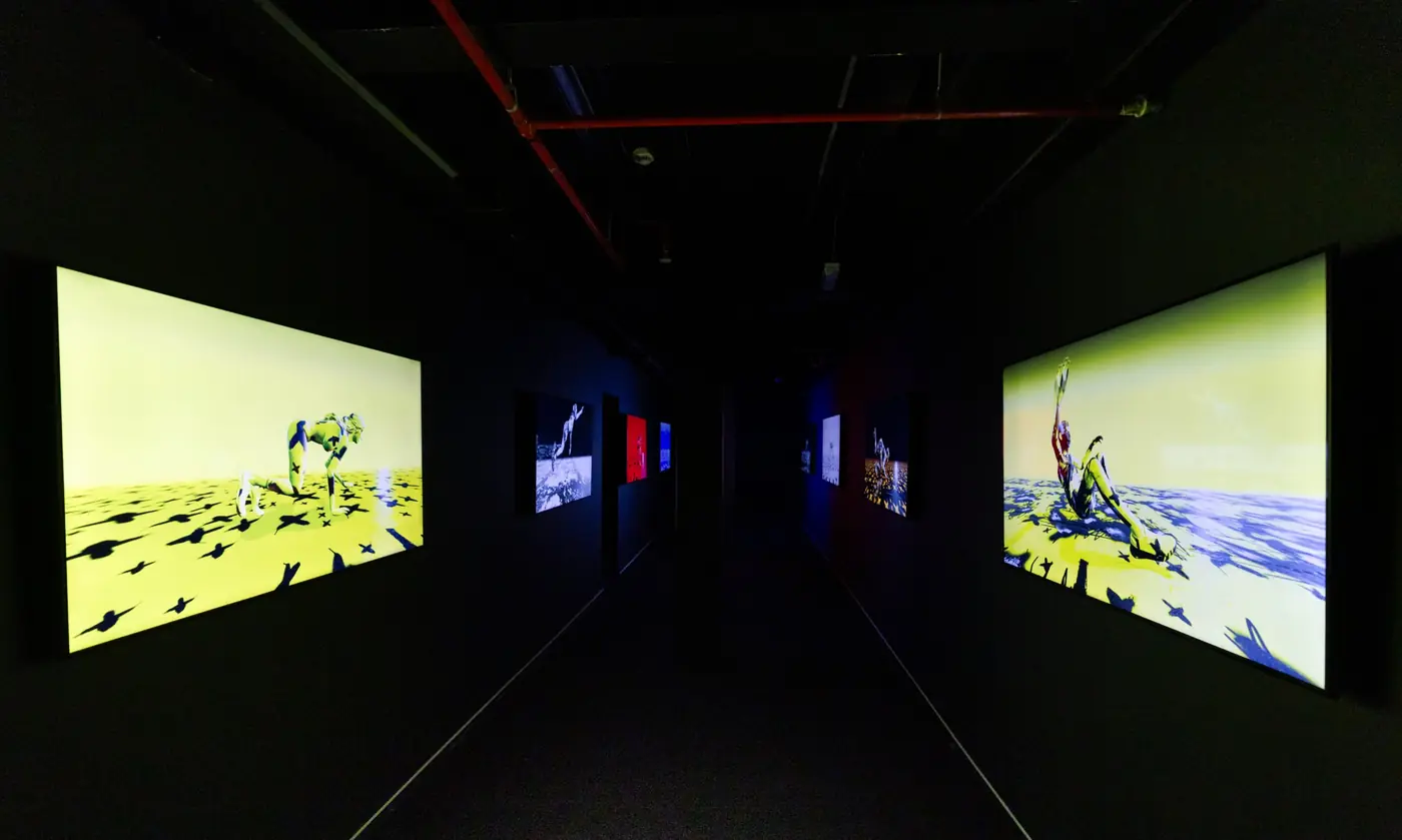A dark corridor lined with large screens showing yellow and blue figures
