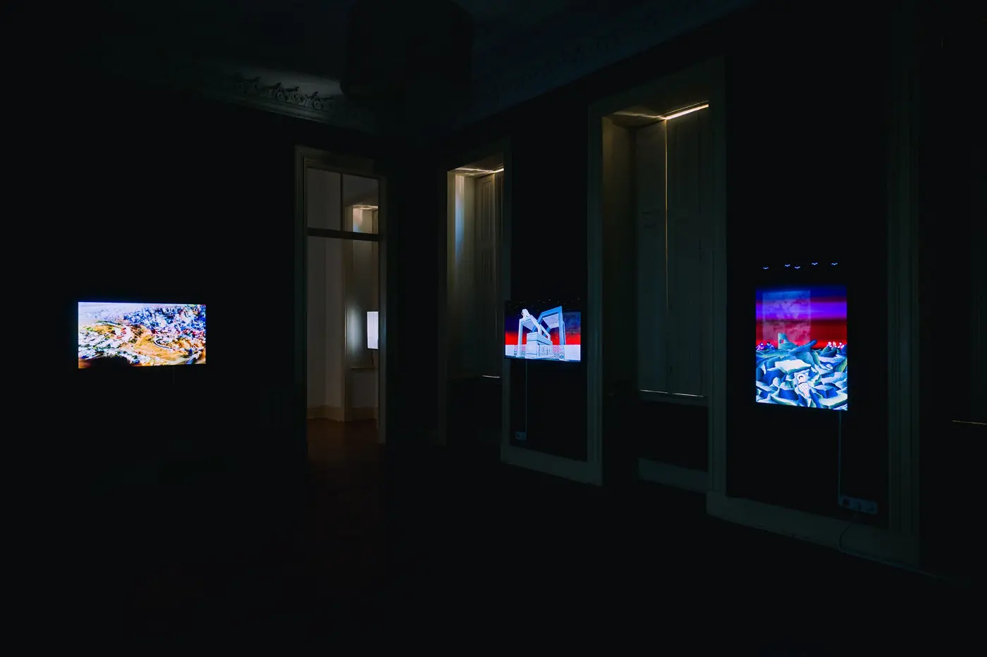 Three glowing screens in a darkened room with tall windows